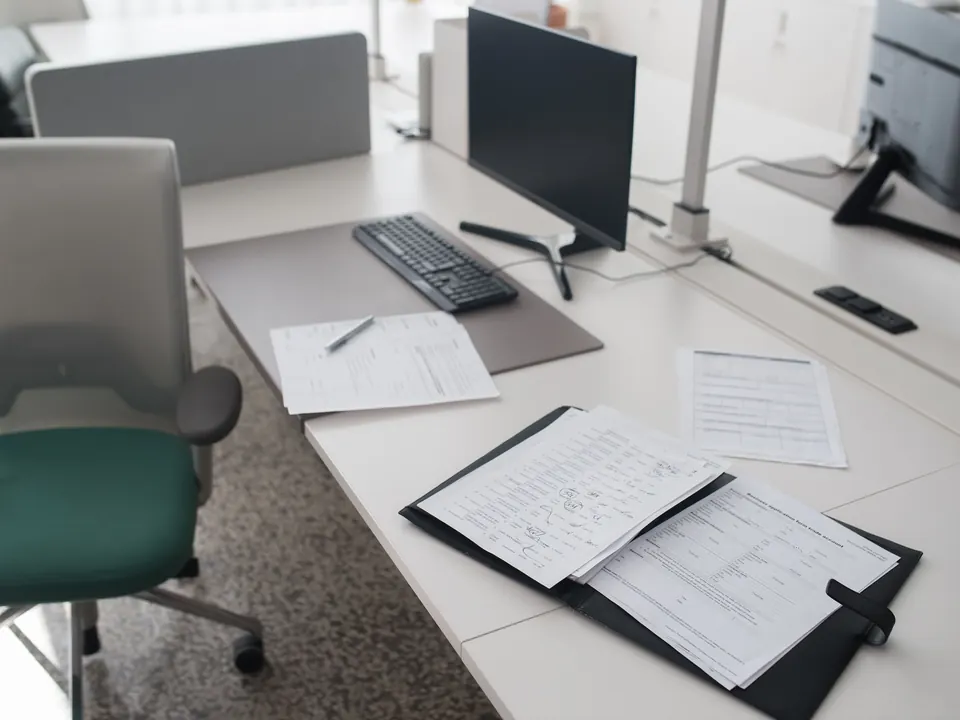 Aufgeräumter Schreibtisch mit Ordner, Formularen und Monitor