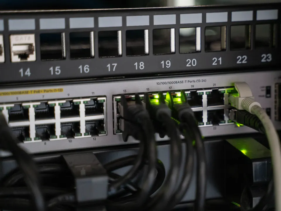 Patchfeld über einem Switch mit gesteckten Netzwerkkabeln und grünen Link-Leuchten