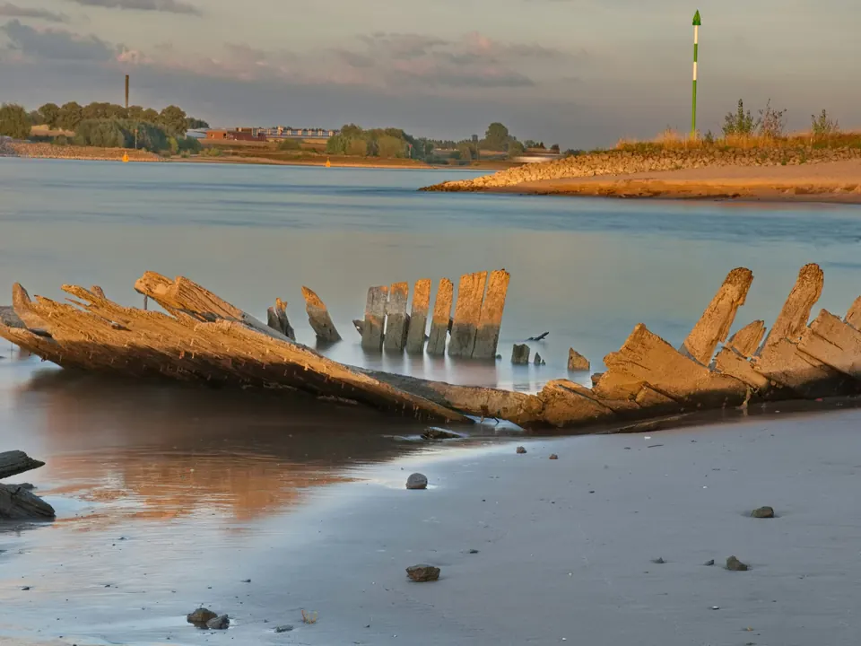 Rheinufer am Niederrhein im Abendlicht, ein altes Schiffswrack ragt bei Niedrigwasser aus dem Sand